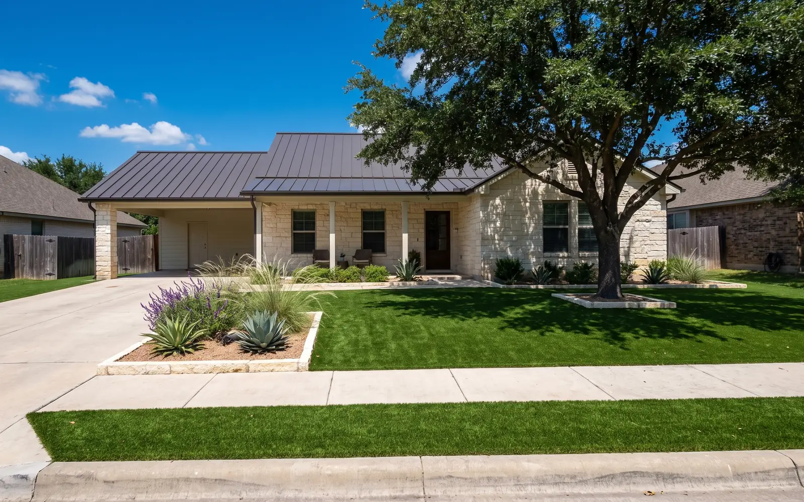 A turf front yard at a limestone house with a live oak and a limestone-edged bed